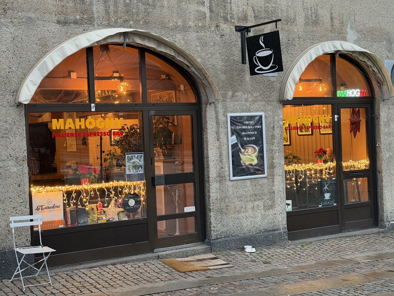 Mahognys två valvfönster på Kapellgatan 10 en kväll, med varmt ljus inifrån och skylten Mahogny italiensk espressobar