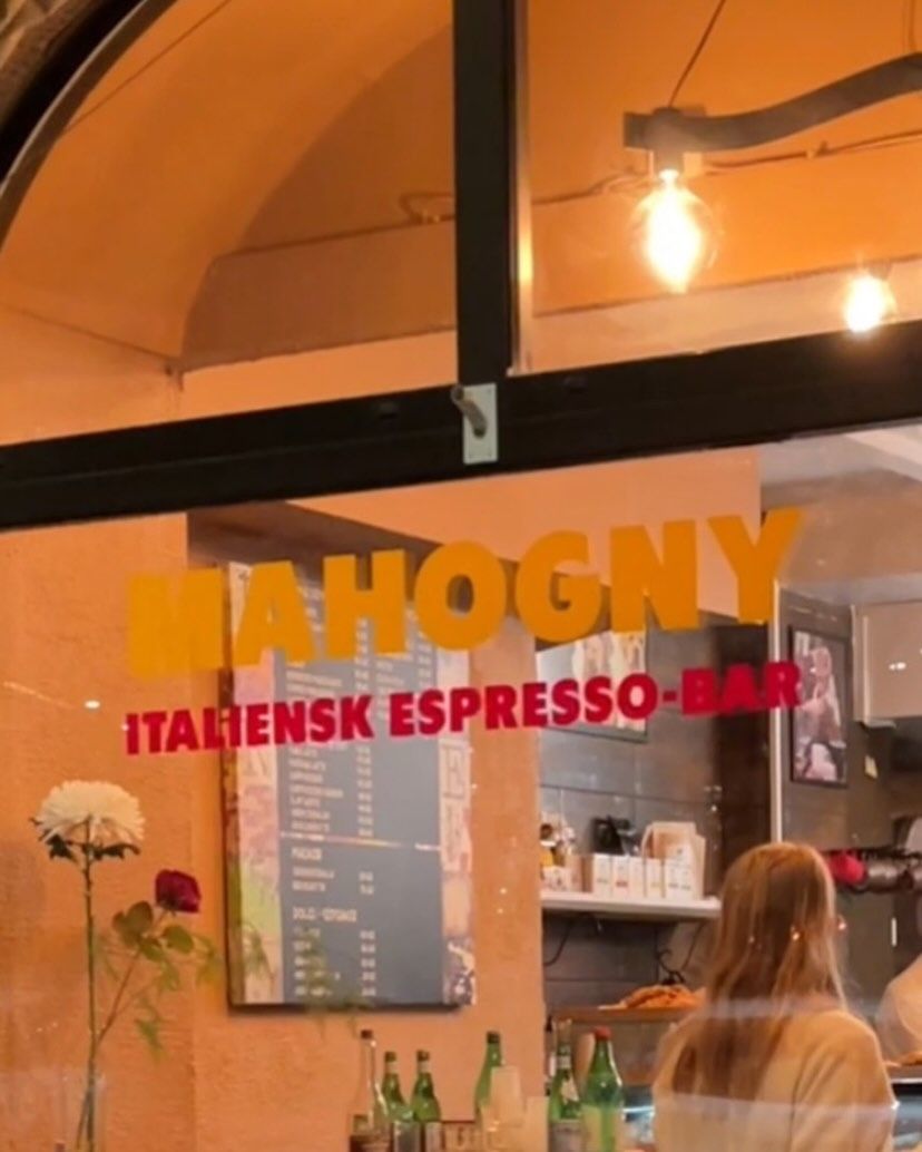 Skylten Mahogny italiensk espresso-bar i fönstret på Kapellgatan, med gatan speglad i glaset